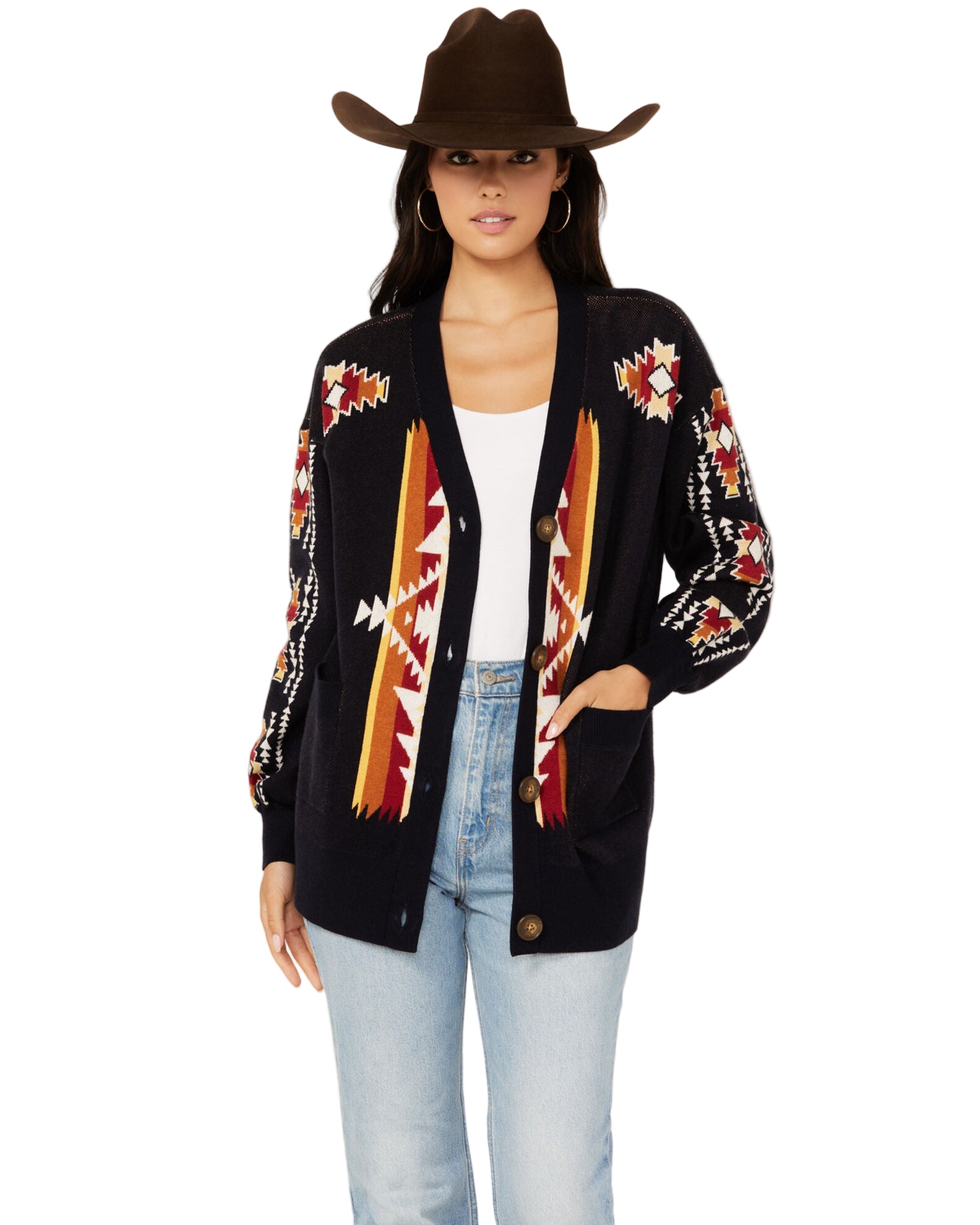 A woman modeling a navy southwestern cardigan with long sleeves and a V-neckline, featuring colorful geometric patterns. She is wearing light blue jeans and has a brown hat on.